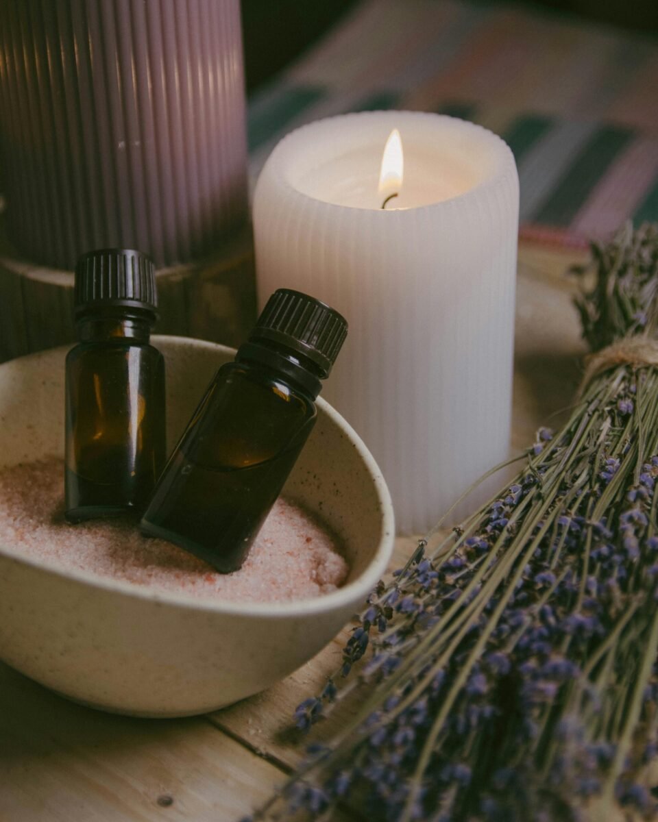 Essential oil bottles resting in a bowl of Epsom salts beside a lit candle